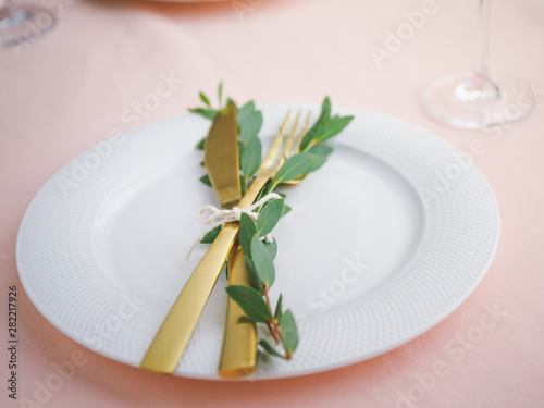 Festive table setting for celebrate event or dinner with white plate and golden cutlery on a pink tablecloth.