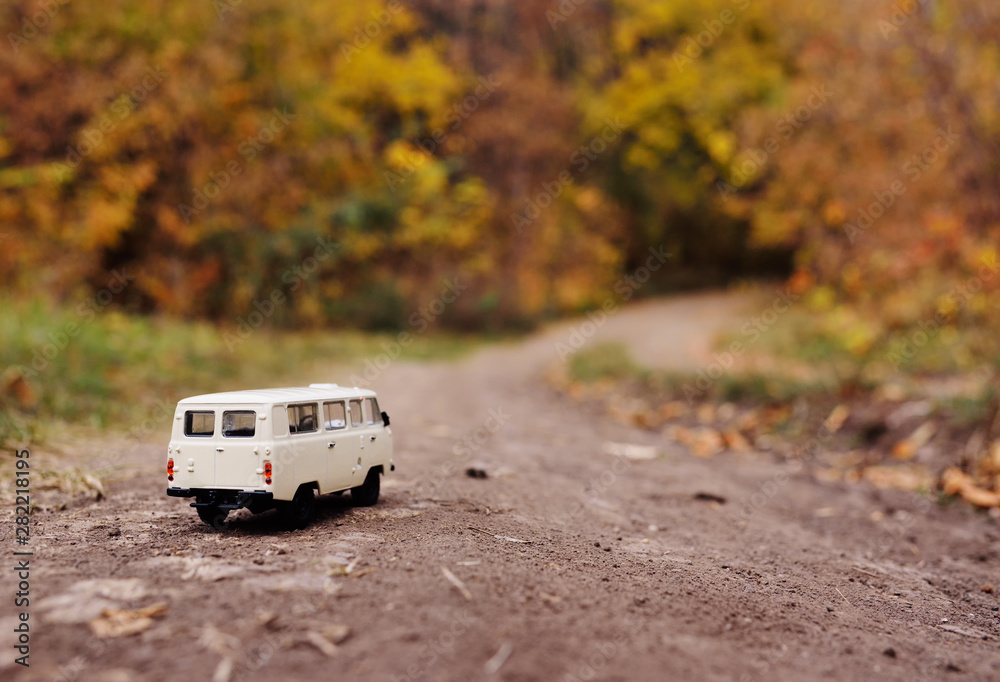 white little toy car rides on the road against the background of autumn yellow trees. Place for text, design blank, copy space, Hello autumn. white little toy car rides on the road against the background of autumn yellow trees. Place for text, design blank, copy space, Hello autumn.