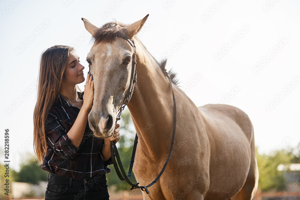 Obraz premium Tenderness, animals and friendship concept. Pretty female jockey, female vet adore horses, petting gently pet foretop, smiling gently, wanna ride along countryside as spending weekend on farm