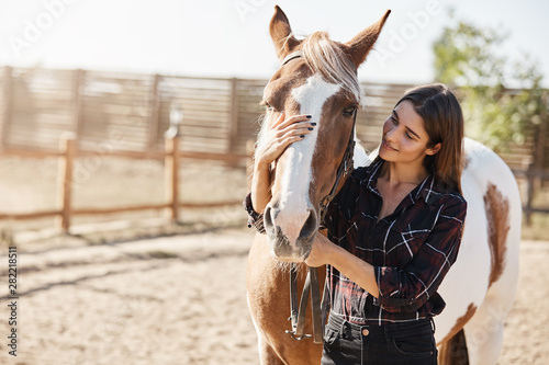 Fotografija Lovely caucasian woman in checked shirt, hugging horse, horsewoman adore her pet, smiling gently, grooming animal as standing on farm near wooden fence in morning