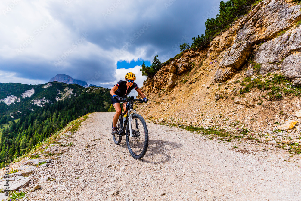 Tourist cycling in Cortina d'Ampezzo, stunning rocky mountains on the background. Woman riding MTB enduro flow trail. South Tyrol province of Italy, Dolomites. Tourist cycling in Cortina d'Ampezzo, stunning rocky mountains on the background. Woman riding MTB enduro flow trail. South Tyrol province of Italy, Dolomites.