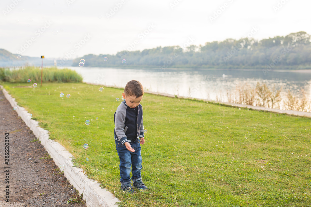 Children and nature concept - Boy trying to catch soap bubbles