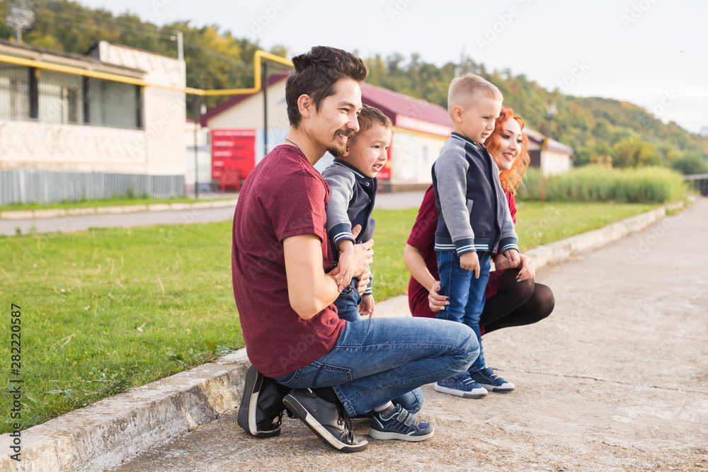 Parenthood, childhood and family concept - Parents and two male children walking at the park and looking on something