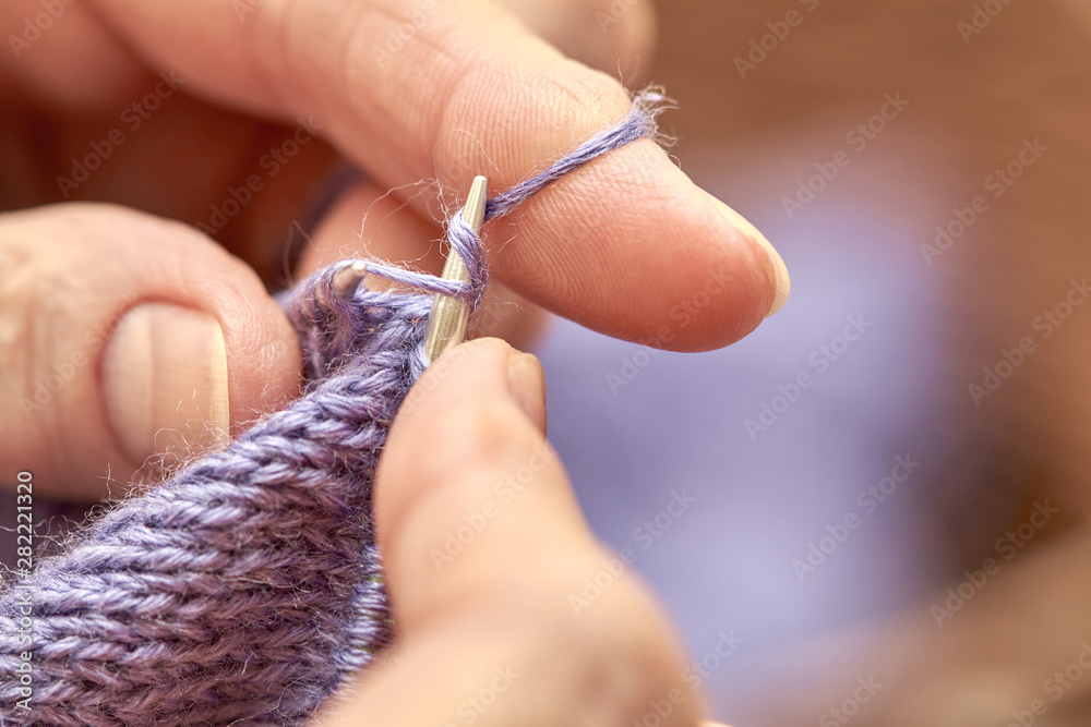 Woman is knitting a blue warm sweater. A hobby of elderly woman is knitting. Closeup view of knitting loop. Selective focus Woman is knitting a blue warm sweater. A hobby of elderly woman is knitting. Closeup view of knitting loop. Selective focus