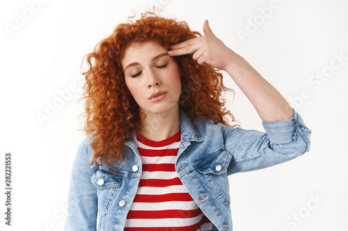 Gosh kill me please. Tired bored redhead feminine young woman close eyes showing finger gun pistol pressed temple head shooting from boredom exhausted standing white background photo