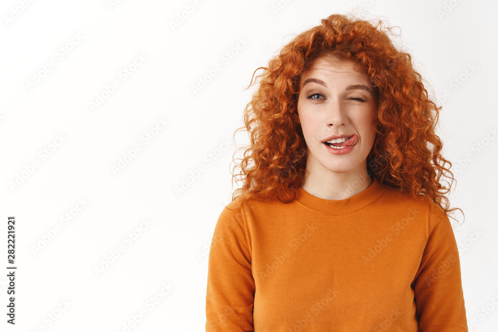 Playful cute stylish redhead curly-haired female student enjoy life, lead active lifestyle, showing tongue and wink joyfully, stay bright side, fool around cheerfully standing white background