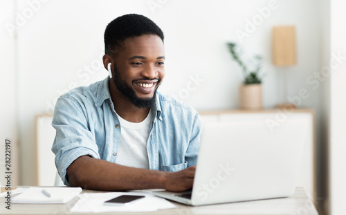 Smiling african-american guy in earphones studying foreign language online photo