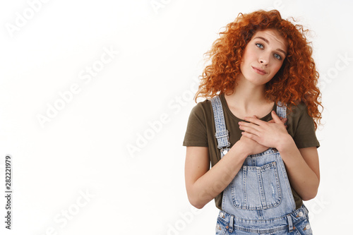 Touched cute modern hipster girl with red curly hair, press hands heart, tilt head sighing romantically, look with admiration, fascinated see breathtaking performance, stand white background