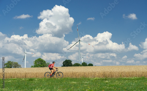 nice, active woman, riding her electric mountain bike between wheat fields and wind wheewls of a wind farm on the Schwaebische Alb near the city of Aalen, BadenWuerttemberg, Germany photo