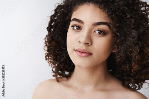 Beauty, salon, self-acceptance concept. Close-up attractive dark curly hairstyle woman standing naked shoulders pure face no flaws smiling look camera relaxed carefree apply night creme skincare