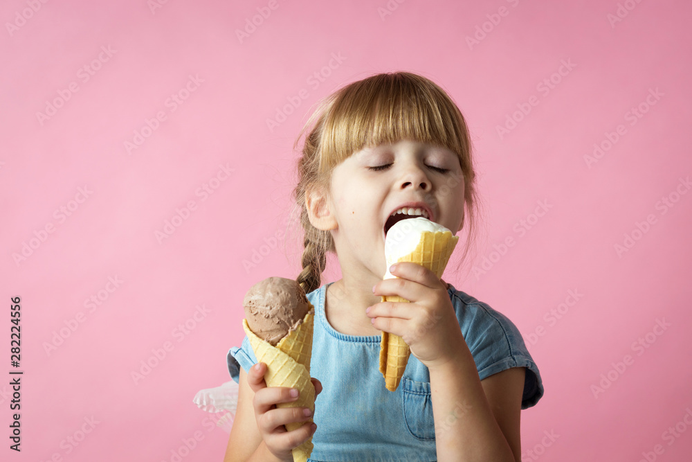 little girl with pigtails in a blue dress eating ice cream in a cone on a pink background - obrazy, fototapety, plakaty 