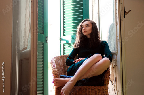 Woman in tight knit dress sitting in wicker chair on a balcony with green wooden shutters in traditional italian hotel. Female solo travel concept Free Download Woman in tight knit dress sitting in wicker chair on a balcony with green wooden shutters in traditional italian hotel. Female solo travel concept - GFXLoad