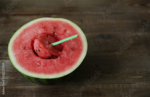 red ripe watermelon with cut out middle on a wooden chopstick on a wooden rustic background with copy space for text