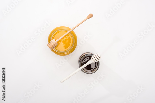 top view of jars with honey and wooden honey dippers on white background with copy space