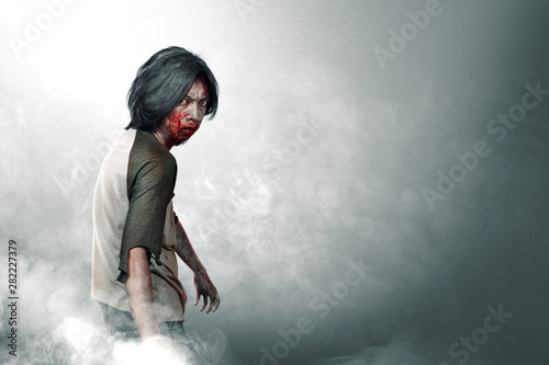 Scary zombies with blood and wound on his body walking amid the fog