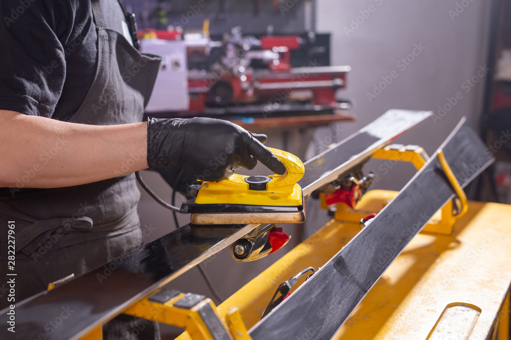 Repair, service and people concept - a man repairing the ski by rubbing a paraffin Repair, service and people concept - a man repairing the ski by rubbing a paraffin