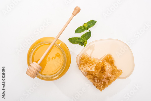top view of jar with honey, mint, honeycomb and wooden honey dipper on white background