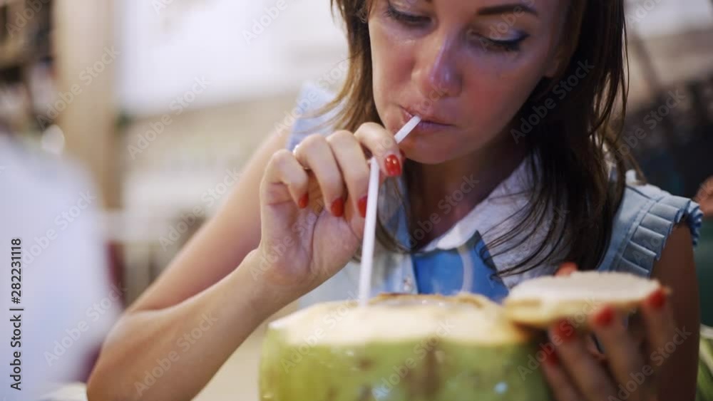 Beautiful female drinks coconut from a straw in a cafe in the evening, close-up. Beautiful female drinks coconut from a straw in a cafe in the evening, close-up.