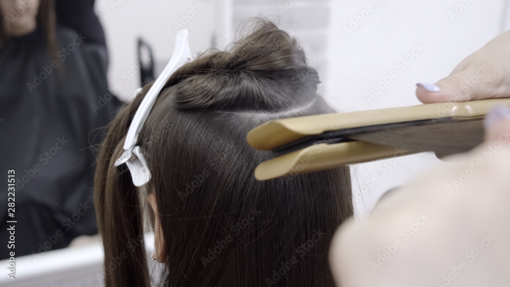 Cute girl with long brunette hair hairdresser doing hair lamination in a beauty salon. concept of hair care treatment Cute girl with long brunette hair hairdresser doing hair lamination in a beauty salon. concept of hair care treatment