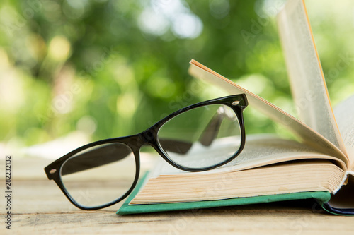 Open book and eyeglasses on a wooden table in a garden. Sunny summer day, reading in a vacation concept