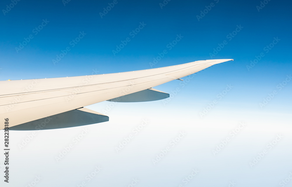 Wing of plane over white clouds. Airplane flying on clear blue sky. Scenic view from airplane window. Commercial airline flight. Plane wing above cloud. Flight mechanics concept. International flight. Wing of plane over white clouds. Airplane flying on clear blue sky. Scenic view from airplane window. Commercial airline flight. Plane wing above cloud. Flight mechanics concept. International flight.