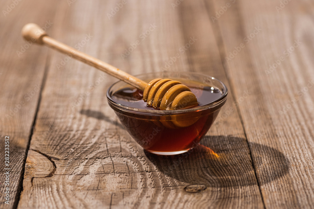 Fototapeta premium glass bowl with honey and honey dipper on wooden table in sunlight