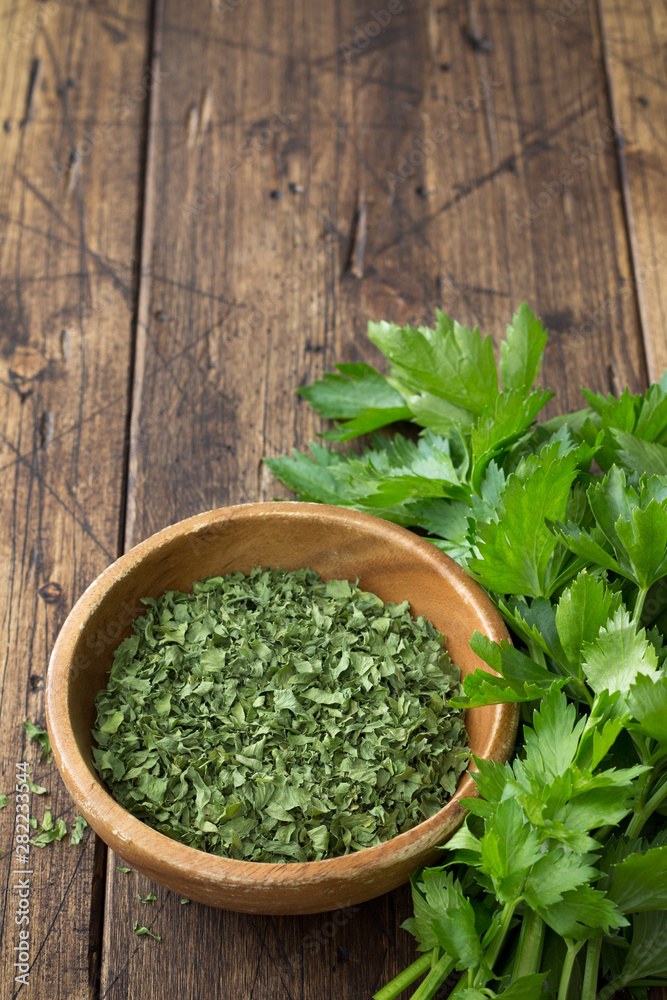 Dried green celery in a wooden bowl and fresh celery on a wooden table Dried green celery in a wooden bowl and fresh celery on a wooden table