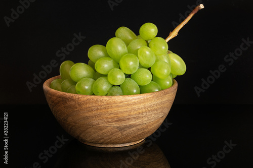 Lot of whole fresh green grape in big wooden bowl isolated on black glass