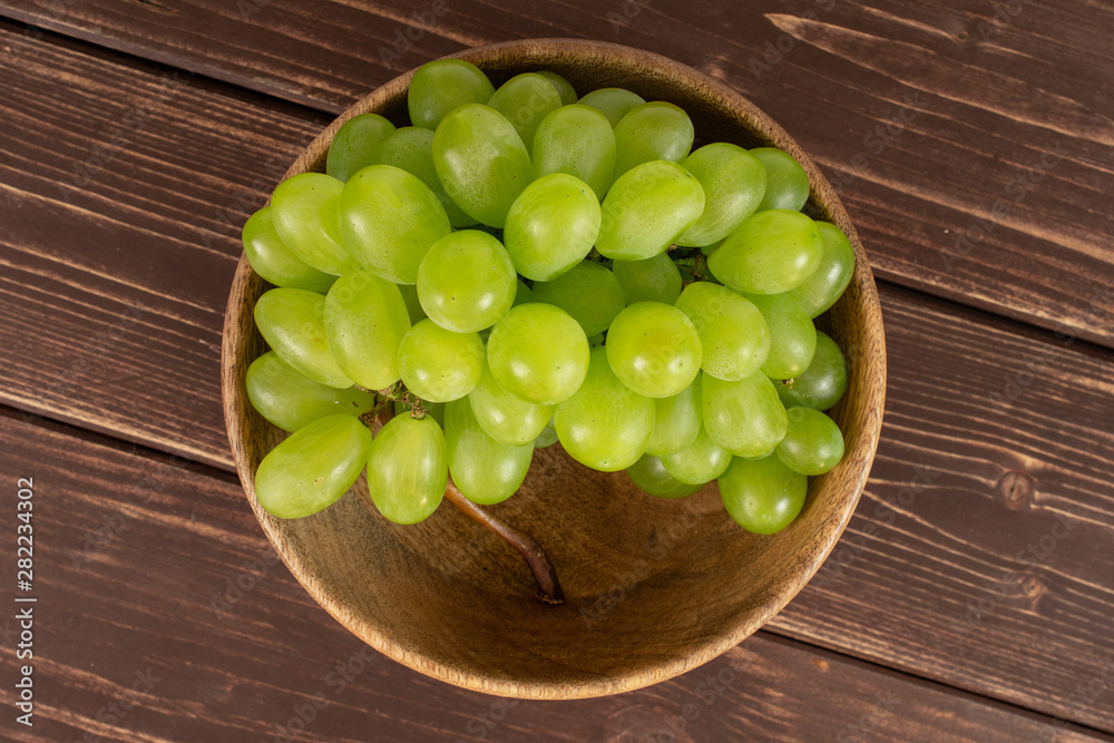 Lot of whole fresh green grape in big wooden bowl flatlay on brown wood Lot of whole fresh green grape in big wooden bowl flatlay on brown wood