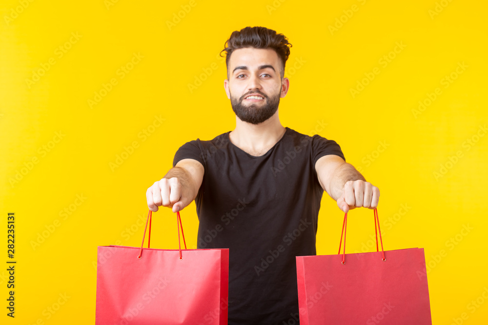 Man is holding red shopping bags on a yellow background. The concept of shopping in the supermarket and gifts. Advertising space.