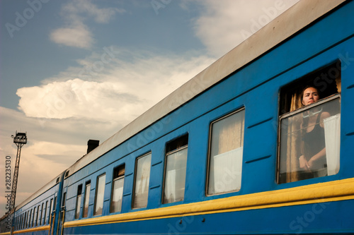 Girl on train. Portrait of passenger in window of blue railway car. Traveling alone by rail. Train in perspective