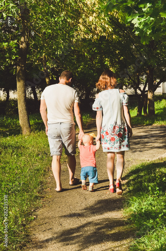 young lovely couple with a little kid, holding hands and walking together in a sunny warm summer day in a city park  © Tetiana Kurian