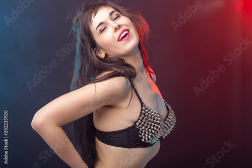 Beautiful young sexy brunette woman posing on a dark background in a riveted top on a dark background. The concept of grooming and attractiveness.