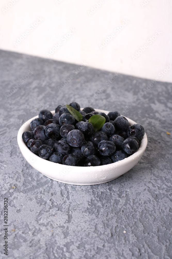 Bowl of tasty fresh blueberries, leaves on grey stone surface, flat lay. Space for text Bowl of tasty fresh blueberries, leaves on grey stone surface, flat lay. Space for text