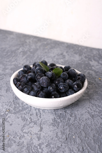 Bowl of tasty fresh blueberries, leaves on grey stone surface, flat lay. Space for text