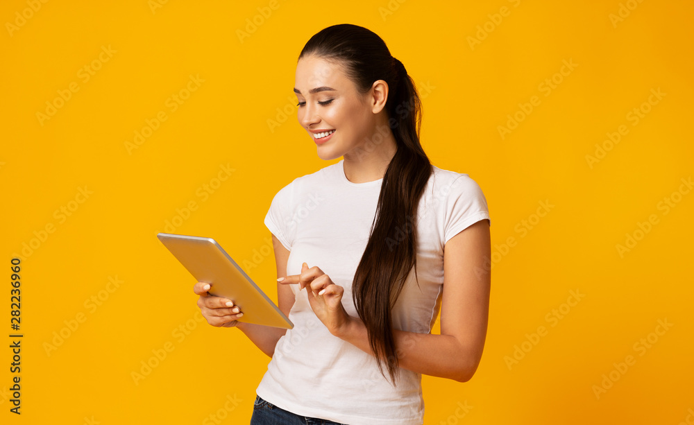 Lovely Girl Using Digital Tablet Over Yellow Studio Background Lovely Girl Using Digital Tablet Over Yellow Studio Background