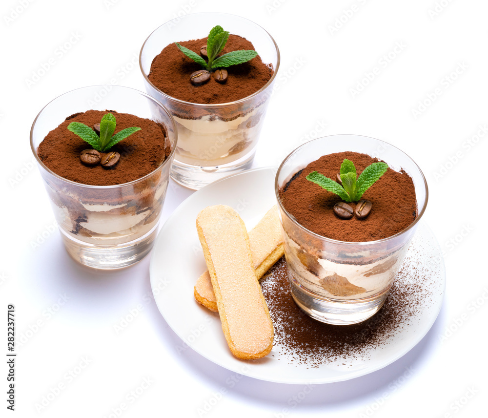 Classic tiramisu dessert in a glass cup and savoiardi cookies on plate with spoon isolated on a white with clipping path Classic tiramisu dessert in a glass cup and savoiardi cookies on plate with spoon isolated on a white with clipping path