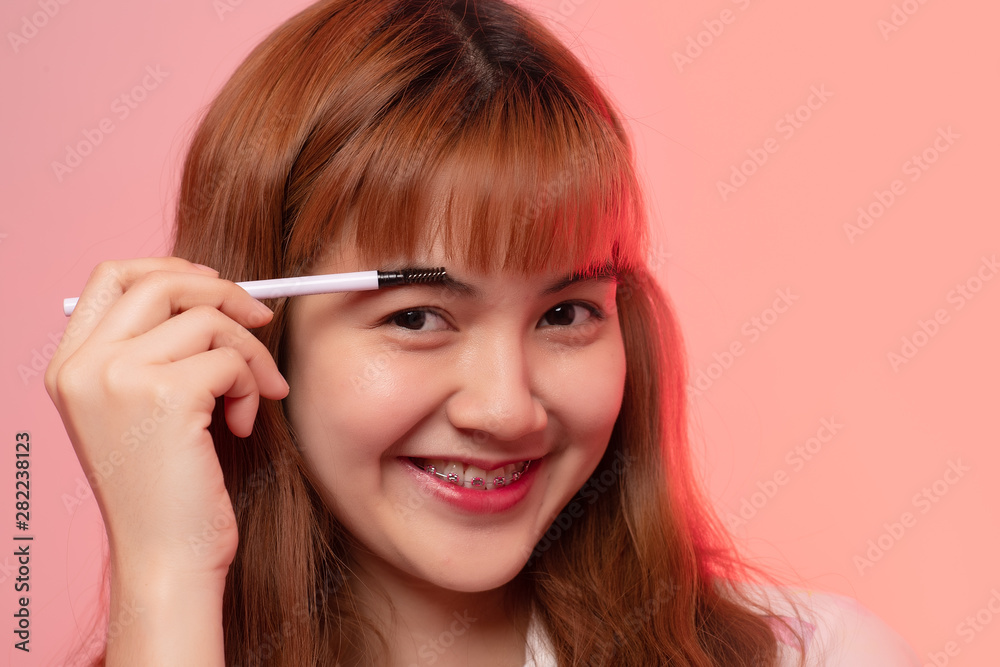 Obraz premium Close-up happy beautiful face of girl applying eyeshadow, Asian woman make up on pink background.
