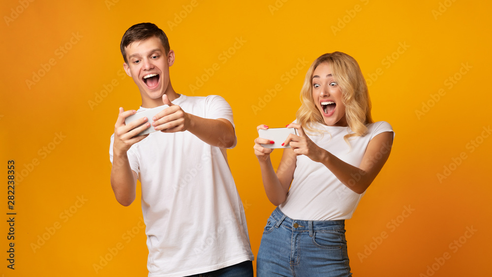 Excited young man and woman playing together on smartphones Excited young man and woman playing together on smartphones
