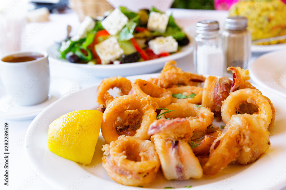 Close-up of fried squids, with greek salad and traditional greek coffee in background. Close-up of fried squids, with greek salad and traditional greek coffee in background.