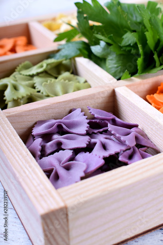 Purple pasta farfalle in a wooden box. Multicolored pasta in the background photo