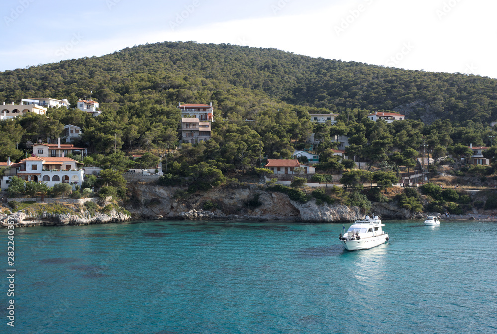 Greece, the pine clad island of Angistri. Pleasure boats near the rocky shore.  Holiday villas on the hillside.