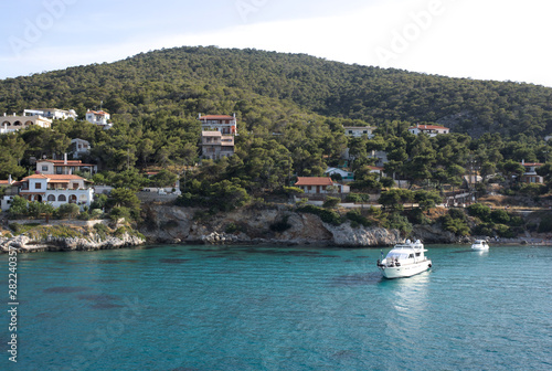 Greece, the pine clad island of Angistri. Pleasure boats near the rocky shore.  Holiday villas on the hillside.