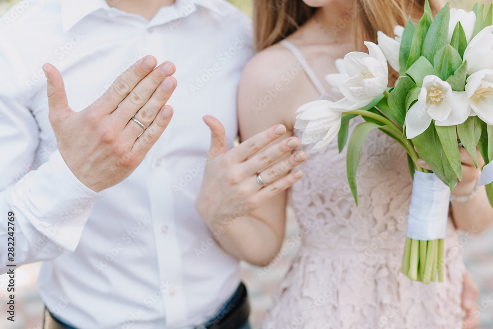 Married Couple Showing Wedding Rings Detailed. Bride in White Dress and Groom in Shirt Partial View. Woman Holding Beautiful Bouquet of Tulip Decorated with Ribbon. Engagement Celebration Married Couple Showing Wedding Rings Detailed. Bride in White Dress and Groom in Shirt Partial View. Woman Holding Beautiful Bouquet of Tulip Decorated with Ribbon. Engagement Celebration