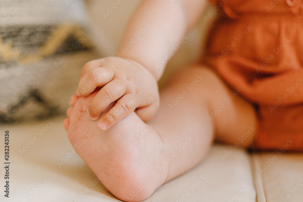 Partial View of New Born Baby Tiny Leg Sitting. Closeup Shot of Adorable Infant Foot on Sofa. Body Part Selective Focus. Little Child Holding Small Toe. Caucasian Toddler Peaceful Picture Partial View of New Born Baby Tiny Leg Sitting. Closeup Shot of Adorable Infant Foot on Sofa. Body Part Selective Focus. Little Child Holding Small Toe. Caucasian Toddler Peaceful Picture