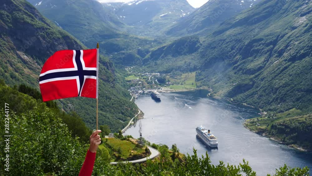 Norwegian flag waving on wind. Fjord Geirangerfjord with cruise ship in the background. View from Ornesvingen viewpoint. Travel for relaxation and sightseeing