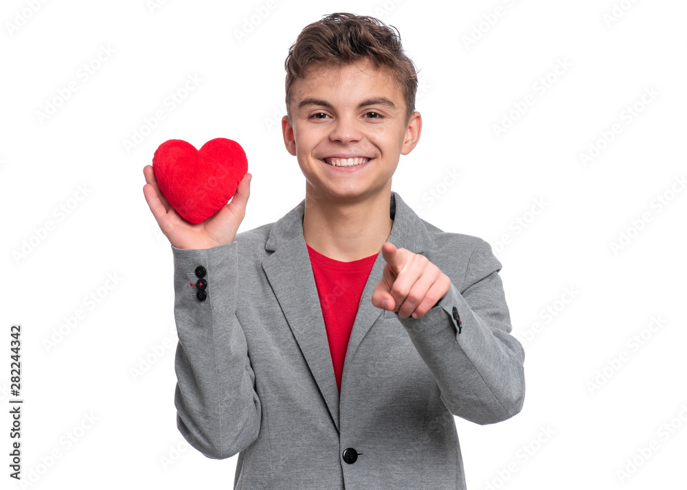 Happy Valentines Day. Cute young Teen Boy in Love with Red plush Heart in his hands. Smiling Child pointing finger to you and looking at camera, isolated on white background. Happy Valentines Day. Cute young Teen Boy in Love with Red plush Heart in his hands. Smiling Child pointing finger to you and looking at camera, isolated on white background.