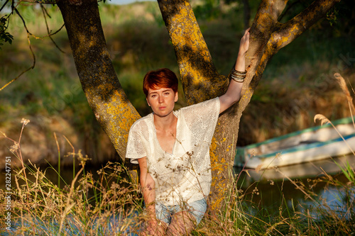 WELL-BEING, WOMAN AGAINST A TREE IN THE GRASS IN THE COUNTRYSIDE