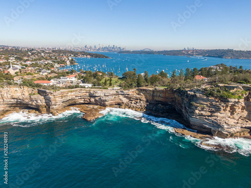 Beautiful aerial drone view of the Gap, an ocean cliff on the South Head peninsula in the suburb of Watson's Bay in eastern Sydney. The central business district of Sydney, Australia in background.