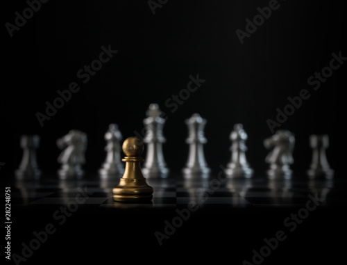 Golden chess pawn is facing the silver opponent chess on black background. Leader, leadership, business strategy, challenge, brave or fearless concept.